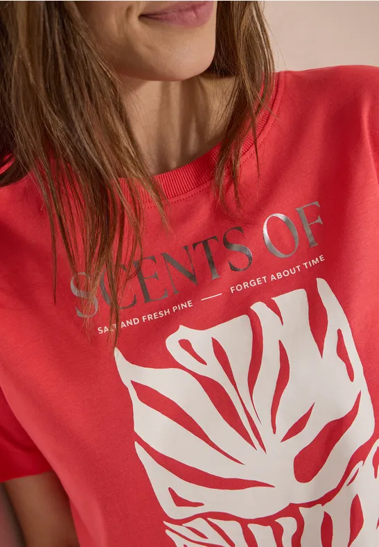 T-shirt rouge avec inscription argentée 'SCENTS OF' et dessin de feuille blanc.