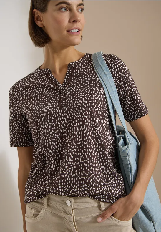 Femme en t-shirt bleu foncé à motifs blancs, manches courtes, pantalon clair et sac bleu à l'épaule.