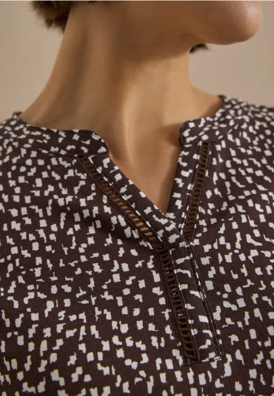 Gros plan sur un haut marron à motif blanc et encolure en V avec détails fantaisie.