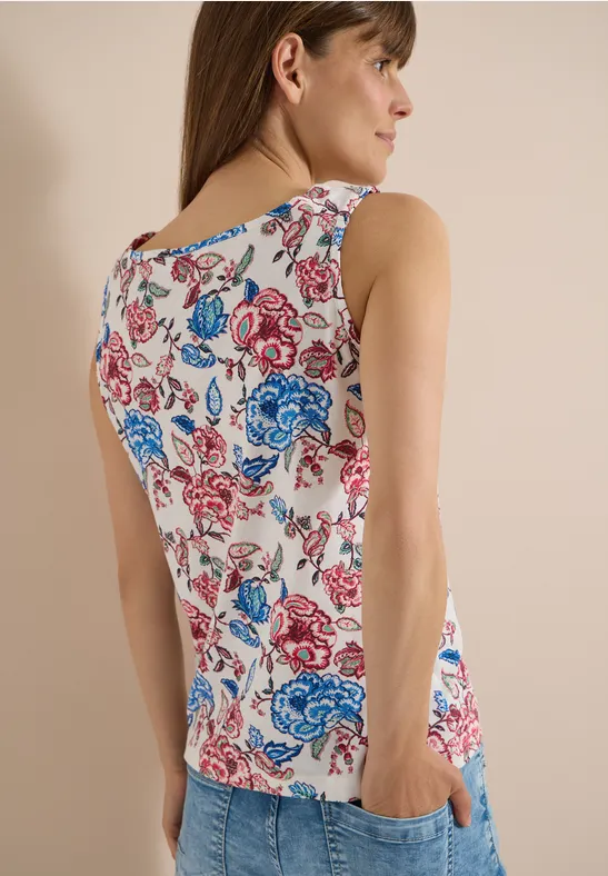 Frau von hinten in ärmellosem Top mit buntem Blumenmuster, Hände in Taschen.