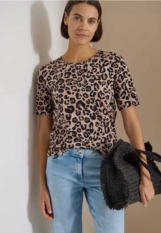 Personne portant un t-shirt léopard beige-noir, jean bleu et grand sac noir tressé, fond neutre.