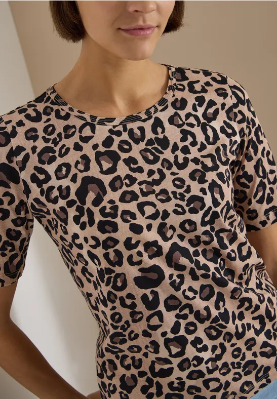 Femme aux cheveux bruns courts portant un t-shirt beige à motif léopard noir.