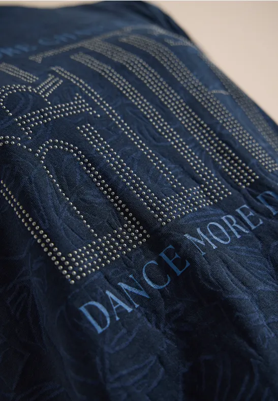 Dunkler Stoff mit gepunktetem Muster und aufgedrucktem Schriftzug „DANCE MORE”