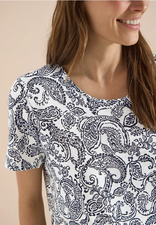 Frau trägt weißes T-Shirt mit dunkelblauem Paisley-Muster, kurzärmelig und lässig.