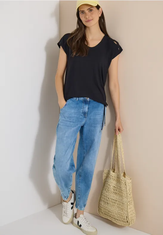 Femme en tenue décontractée : T-shirt bleu foncé, jean ample, baskets blanches et sac en paille.