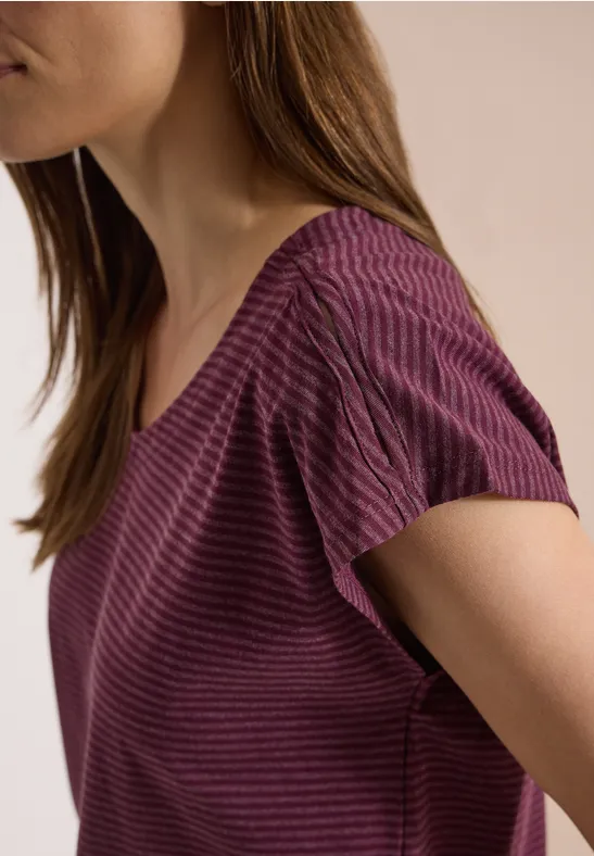 Plan rapproché d'une femme portant un t-shirt violet à rayures, seuls le cou et l'épaule sont visibles.