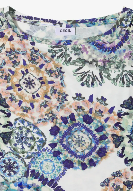 Blouse blanche avec imprimé floral mosaïque multicolore en tons bleus, verts et orangés.