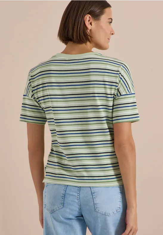Vue de dos d’une femme portant un T-shirt rayé vert-blanc-bleu et un jean clair sur fond neutre.