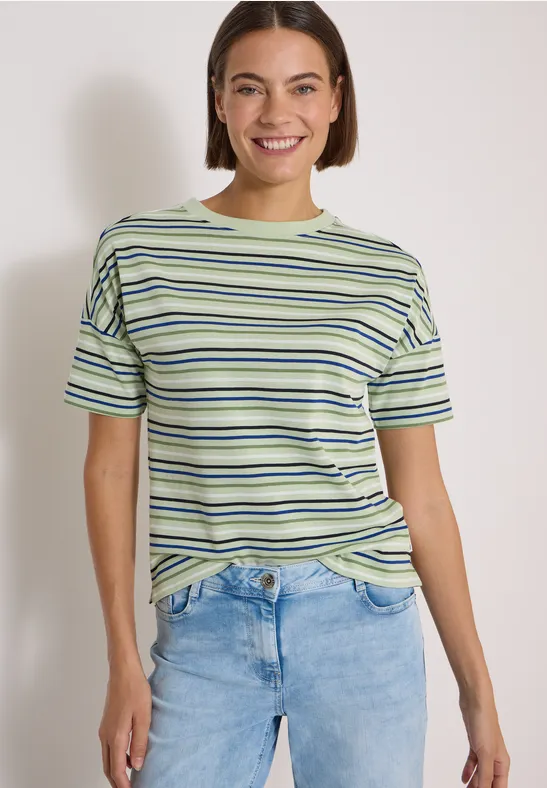 Femme souriante portant un t-shirt rayé et un jean devant un fond clair.