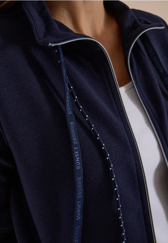 Nahaufnahme einer Person in dunkelblauer Zip-Jacke über weißem Top.