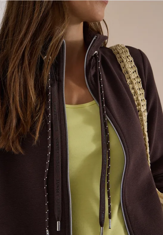 Frau trägt braune Jacke, hellgrünes Top und Häkel-Taschenriemen.