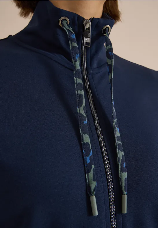 Nahaufnahme eines dunkelblauen Hoodies mit hohem Kragen, Camouflage-Kordeln und Reißverschluss.