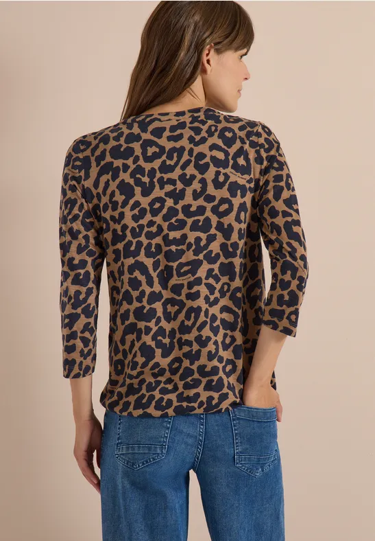 Frau von hinten in blauer Jeans und dreiviertelärmligem Oberteil mit braun-schwarzem Leopardenmuster.