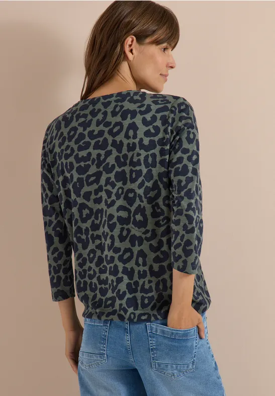 Frau im Leopardenprint-Pullover mit 3/4-Ärmeln und blauen Jeans, Rückansicht.