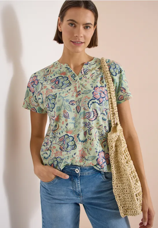 Femme porte un top à motifs floraux, jean bleu et un sac en paille.