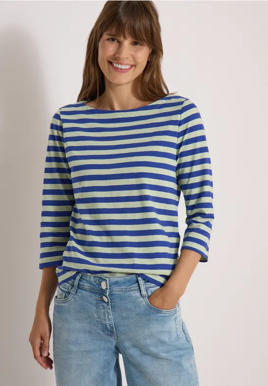 Une femme souriante porte un t-shirt à rayures bleu et blanc avec un jean.