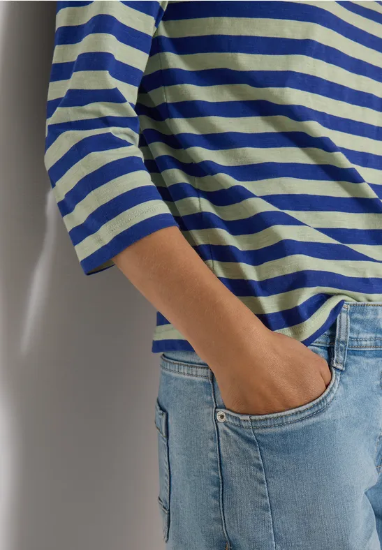 Personne porte un t-shirt rayé bleu et blanc à manches 3/4 et un jean, main dans la poche.