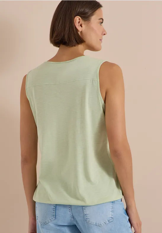 Femme vue de dos portant un débardeur vert clair et un jean bleu sur fond beige.