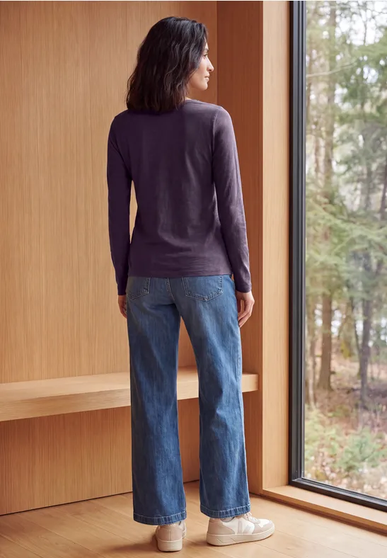 Vue de dos d'une personne en jeans et haut à manches longues, debout près d'une fenêtre et regardant la forêt.