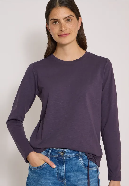 Femme portant un pull manches longues violet foncé et un jean sur fond clair.
