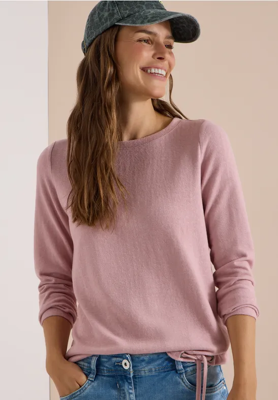 Jeune femme souriante portant un pull rose et une casquette, regard de côté.