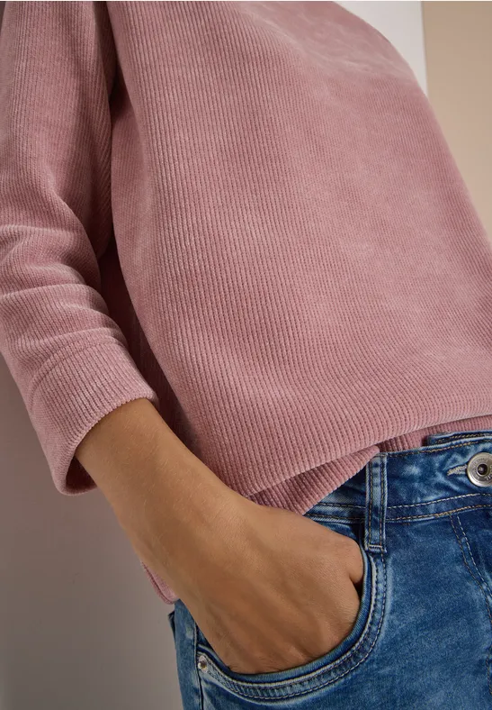 Gros plan d'une personne portant un pull rose et un jean bleu, main dans la poche.