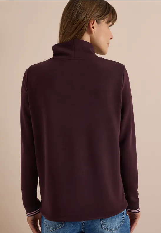 Rückenansicht einer Person in dunkellila Rollkragenpullover und blauer Jeans.