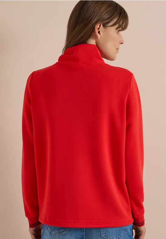 Frau von hinten in roter Fleecejacke mit Stehkragen vor beigem Hintergrund.