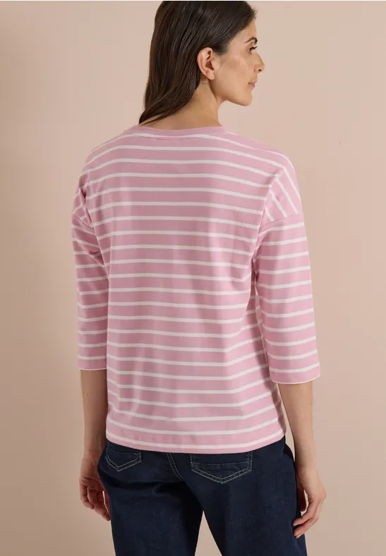Femme de dos portant un haut à manches 3/4 rayé rose et blanc et un jean.