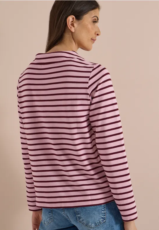 Une femme vue de dos porte un t-shirt rose à rayures noires et un jean bleu.