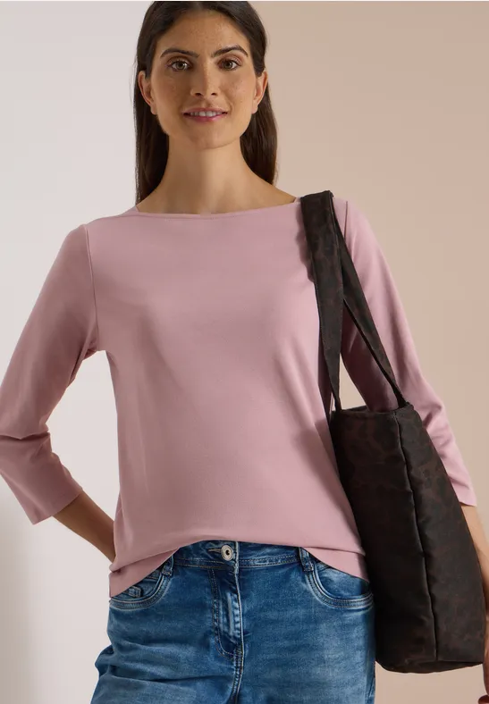 Femme en haut rose, jean et sac noir sur fond neutre.