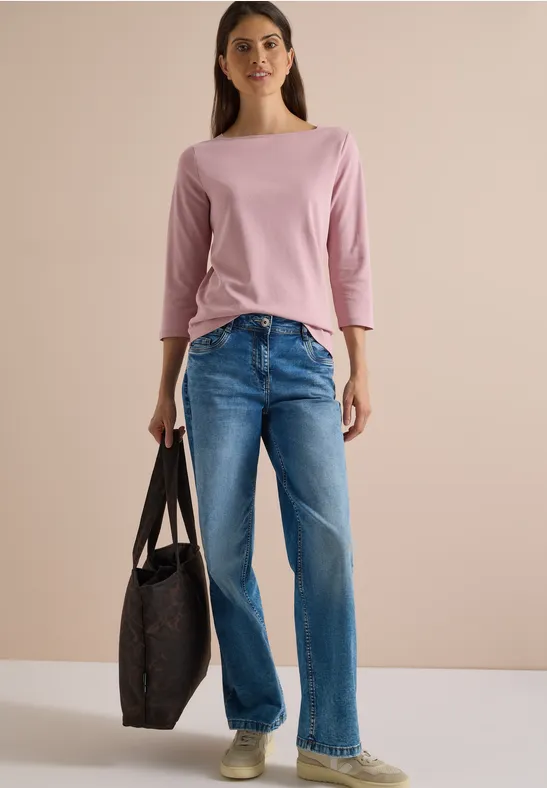 Une femme avec un t-shirt rose à manches trois-quarts et un jean bleu tient un grand sac sombre.