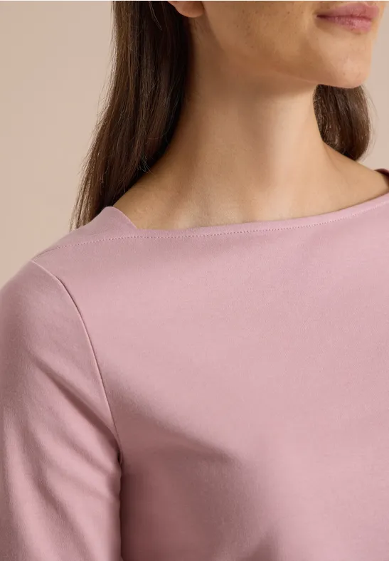 Gros plan d’une femme portant un haut rose pâle à encolure bateau et tissu lisse.