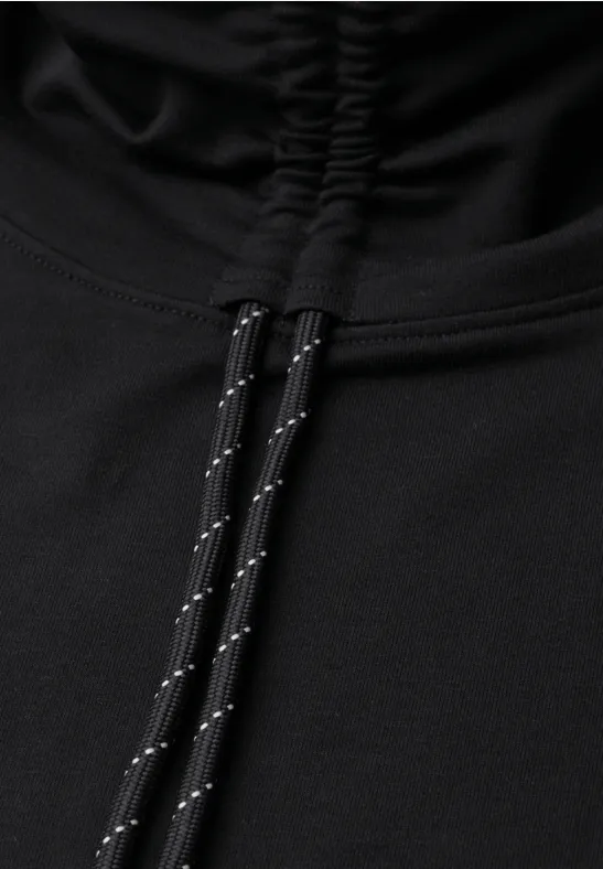 Gros plan sur un vêtement noir avec capuche froncée et cordons noirs à motifs réfléchissants.