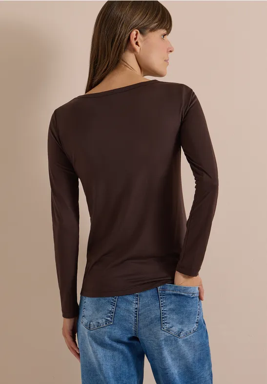 Femme de dos portant un haut marron à manches longues et un jean bleu.