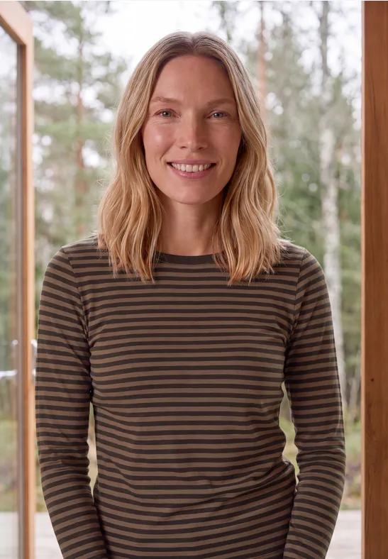 Femme souriante en t-shirt à manches longues rayé devant un fond de forêt.