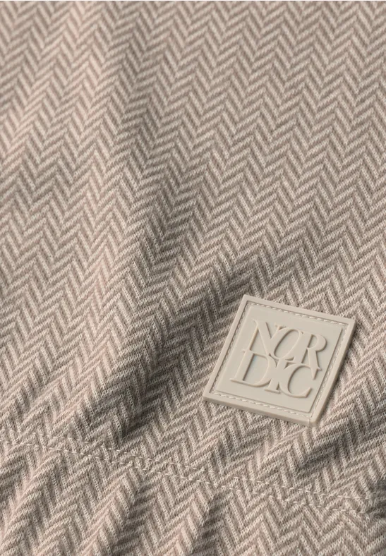 Beige Stoff mit Fischgrätmuster und eingenähter quadratischer Logo-Patch mit geprägten Buchstaben.