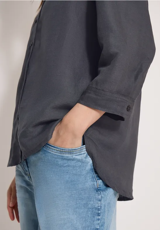 Schwarze Bluse über blaue Jeans, Hand lässig in der Hosentasche.