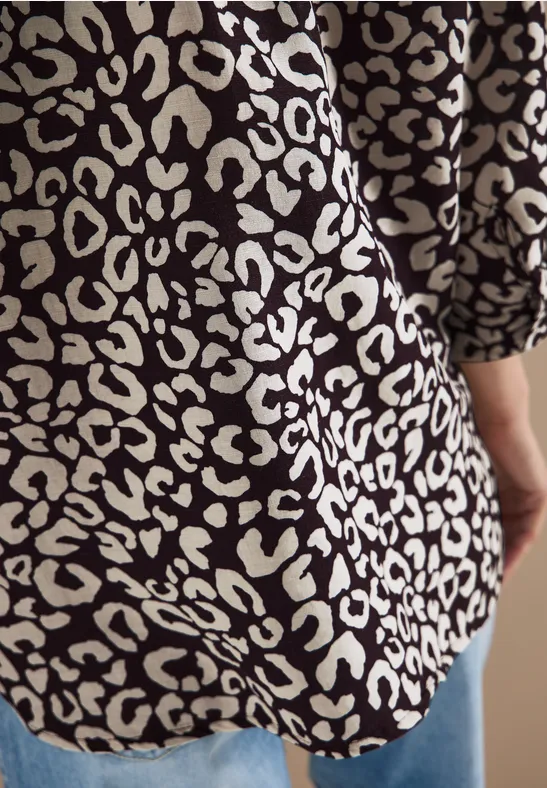 Rückansicht einer Person in schwarzem Blusen-Shirt mit cremefarbenem Leoprint und blauen Jeans.