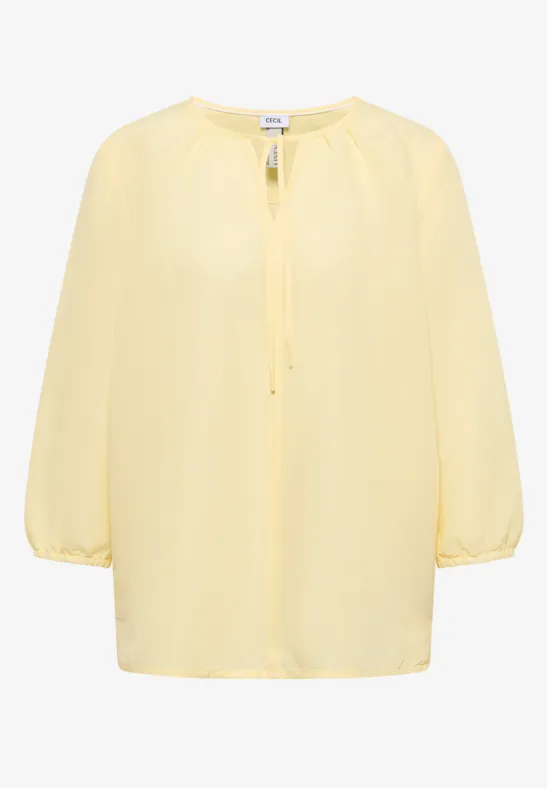 Blouse légère jaune à manches 3/4 et encolure ronde froncée.