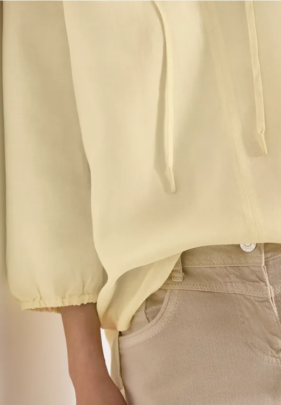 Gros plan sur une personne portant un pull jaune clair à cordon et un pantalon beige.