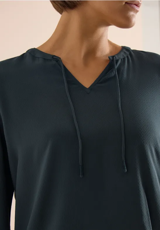 Eine Person trägt ein dunkelblaues Langarmshirt mit V-Ausschnitt und Kordelzug.