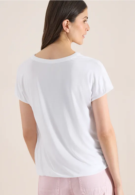 Rückansicht einer Frau mit langem dunklem Haar und weißem T-Shirt vor neutralem Hintergrund.