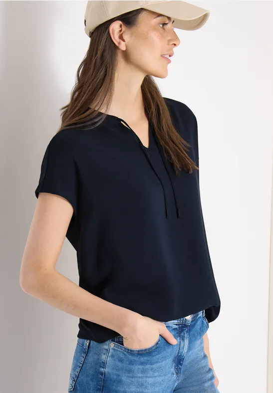 Frau trägt dunkelblaues Poloshirt und blaue Jeans, lässiger Look.