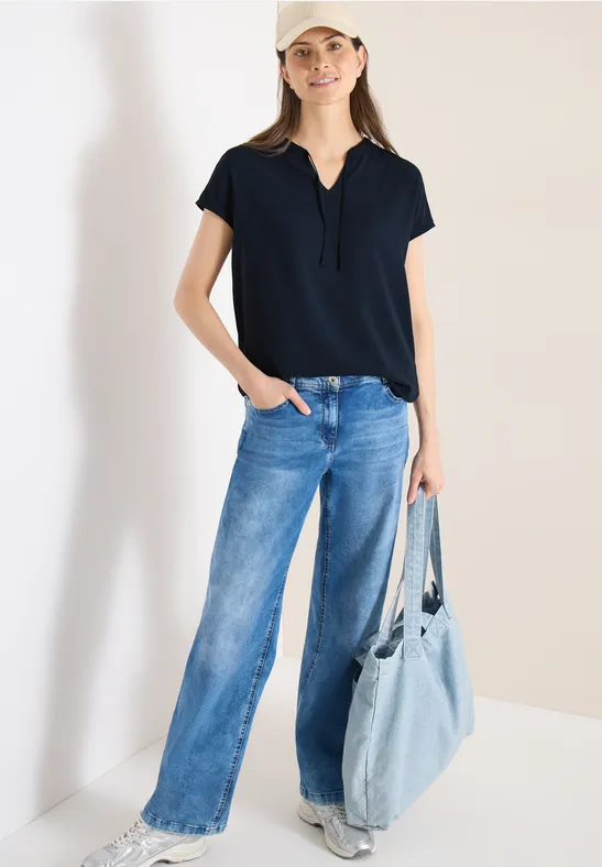 Frau in schwarzem T-Shirt, weiten Jeans und großer hellblauer Umhängetasche.