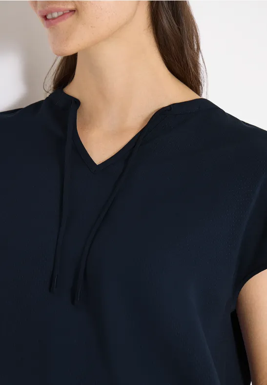 Frau trägt dunkelblaues Shirt mit kurzem Ärmel, V-Ausschnitt und Kapuzenbändern.