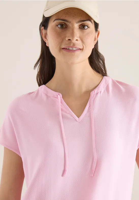 Femme en haut rose pâle à manches courtes, encolure en V et cordons.
