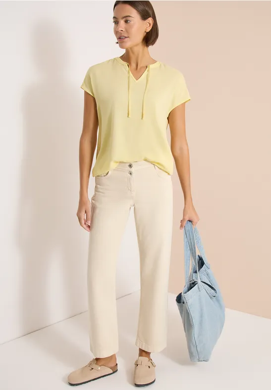 Frau in gelbem Kapuzen-Shirt, heller Hose, beigen Schuhen und hellblauer Stofftasche