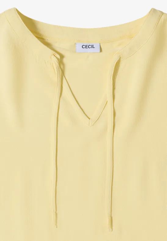 Hellgelbes Damen-Shirt mit V-Ausschnitt und Kordelzug, kurzärmelig, Label 'CECIL' an der Rückseite des Kragens.
