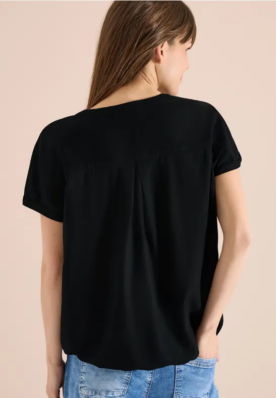 Frau von hinten in schwarzem T-Shirt und blauen Jeans vor neutralem Hintergrund.